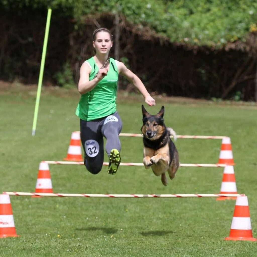 Nina Cappello und ihr Hund springen beim Tunierhundesport gemeinsam über eine Hürde